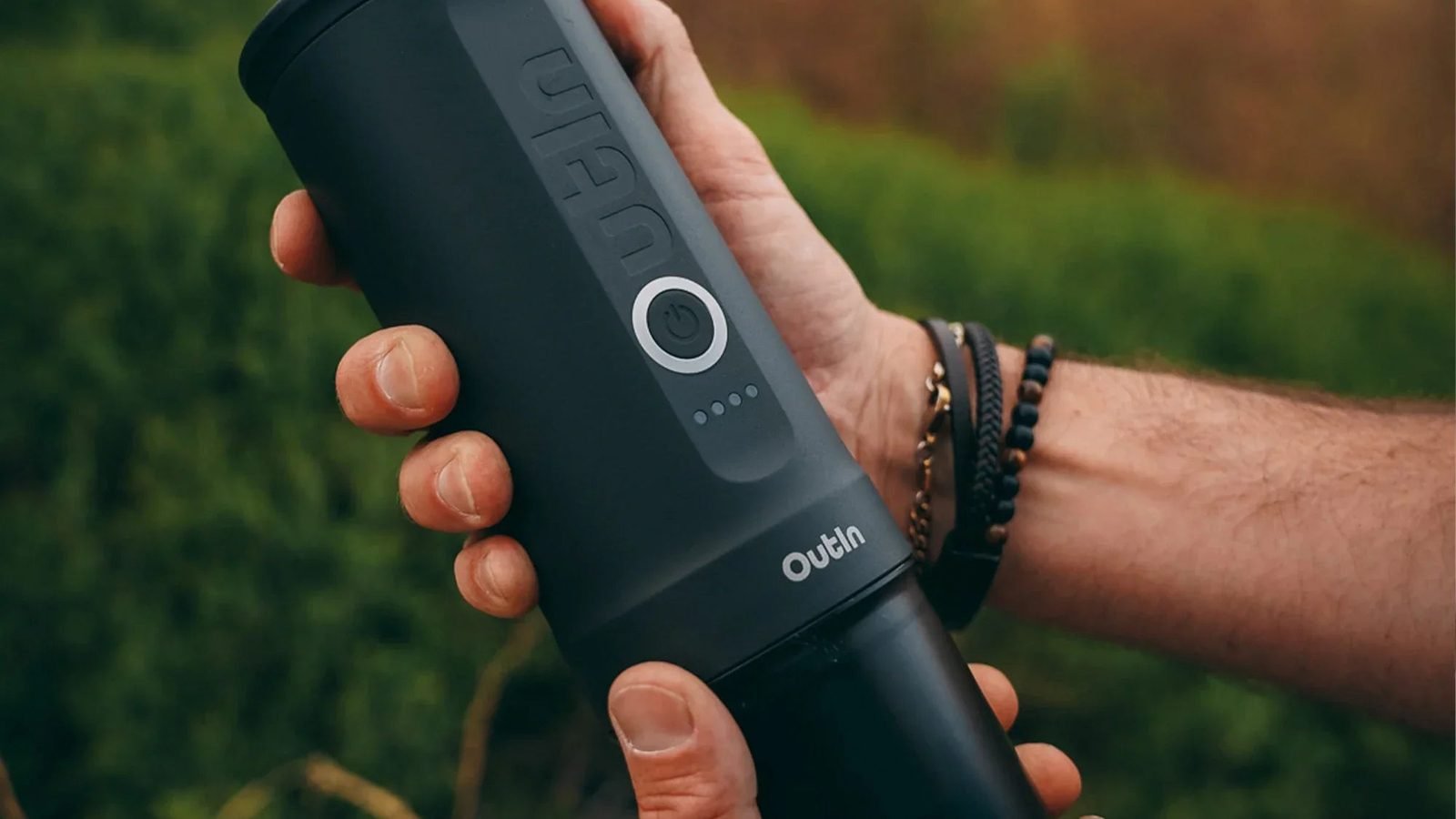 Hands holding a black OutIn Nano 2 portable espresso machine outdoors